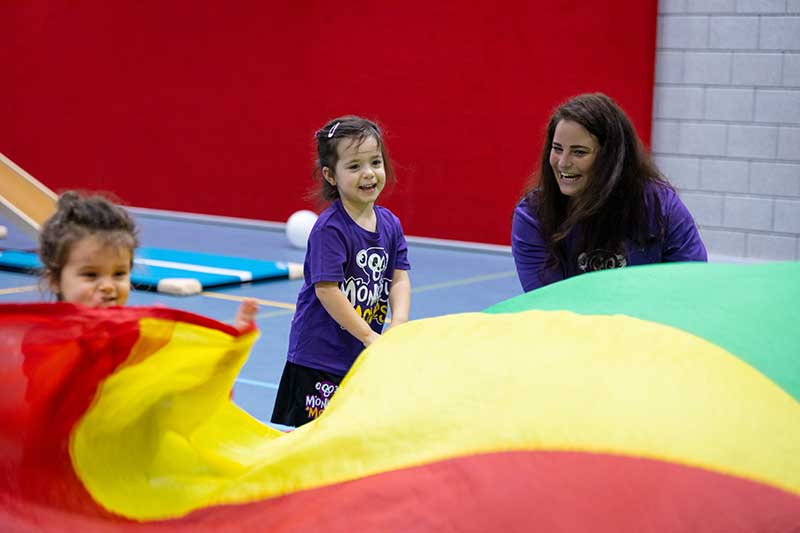 Een Monkey Moves docent speelt met een kind en een kleurrijke parachute